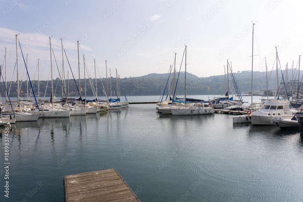 Obraz premium Marina with moored sailboats and masts on calm water. Wooden dock in foreground, hills in background. Wide horizontal composition with copy space