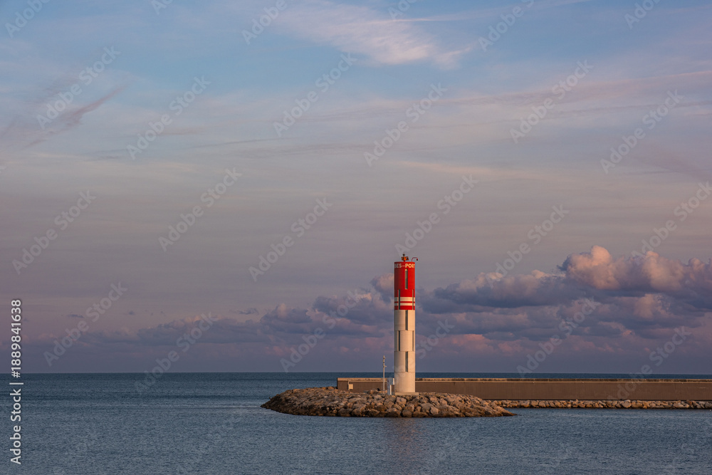 Fototapeta premium White and red lighthouse on a rocky pier at the entrance to Port Vauban in Antibes, French Riviera, France