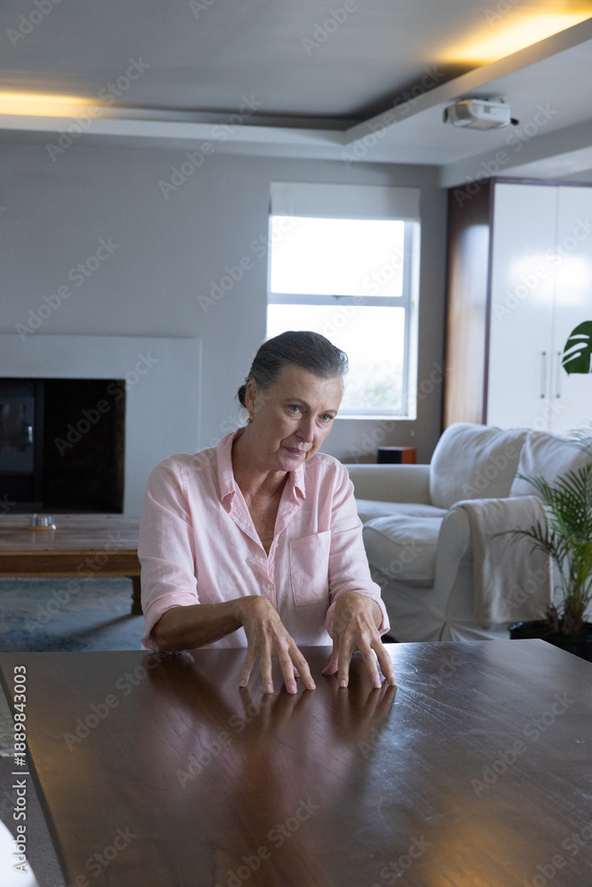Obraz premium Senior woman sitting at wooden dining table wearing shirt in living room with projector
