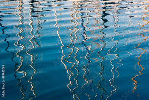 Abstract, wavy reflections of sailboat masts in the deep blue water of a marina, creating a natural artistic pattern.