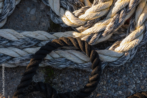Close-up of thick mooring ropes coiled on a concrete pier in a harbor at sunset.