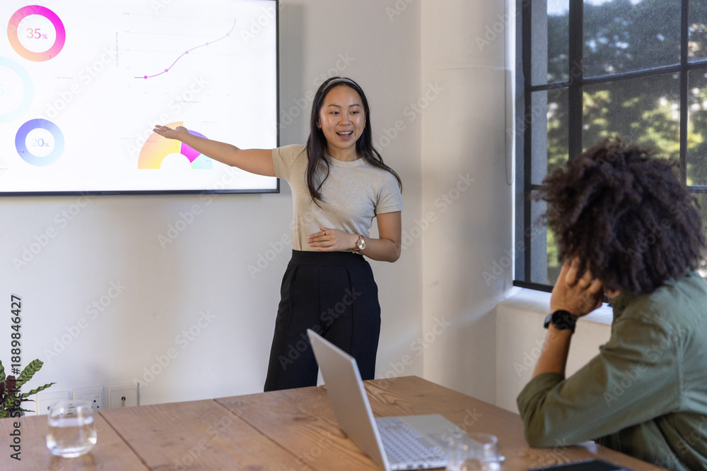Fototapeta premium Diverse coworkers presenting charts on wall-mounted display screen in meeting room, laptop