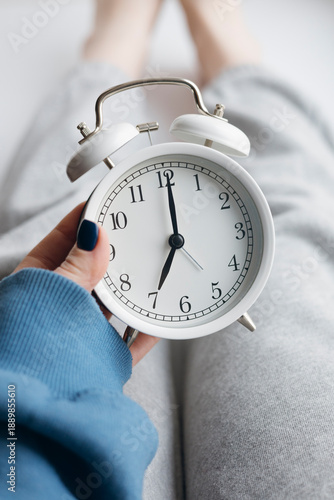 Woman holding alarm clock in bed during morning wake up.