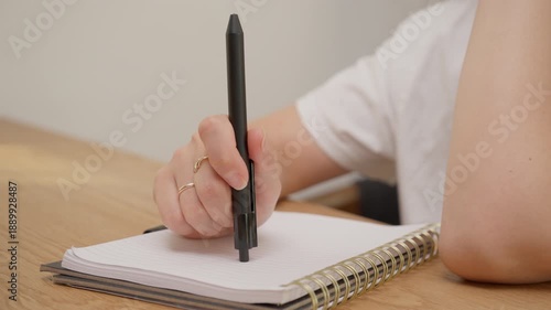 Woman hand hitting pen top on notebook paper at wooden desk. Concept of writer block, frustration or thinking process during business or education. Original sound of tapping hits is included.