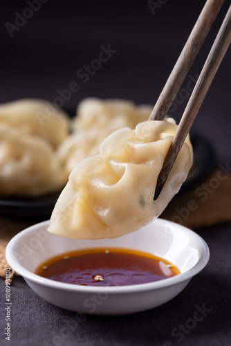Close up of delicious steamed dumplings being dipped into sesame oil sauce with chopsticks
