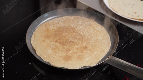 Hand using spatula to flip pancake on frying pan on induction stove. Cooking delicious breakfast or dessert at home with sizzling audio sound of frying dough on hot surface in kitchen.
