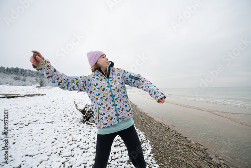 Girl throws a stone into the sea while standing on the snowy shore of a scenic sea in winter.