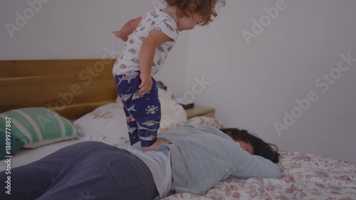 Toddler trying to stand on mother’s back during playful morning moment showing joyful childhood wobbling, warm family bond, and lively real-life interaction
