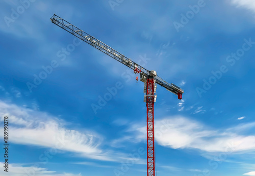 Crane construction work takes place under blue sky during the daytime with clouds in the background