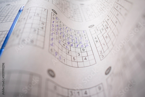 Curved paper pages of a sudoku puzzle book with completed number grids and a blue pen