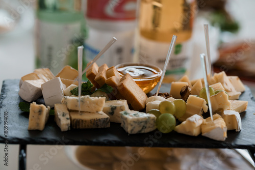 Gourmet Cheese Platter with Honey and Grapes on Black Slate Serving Board with Drinks in Background