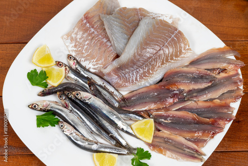 Raw mixed fish on a white plate. Fillets of saithe and anchovies. Flat lay. Closeup.