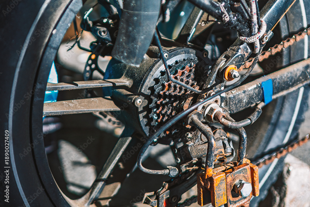 Obraz premium Bicycle drivetrain on an urban street, showing chain, cassette, and rear derailleur in gritty detail. Industrial textures and wear highlight cycling, mechanics, and everyday transport