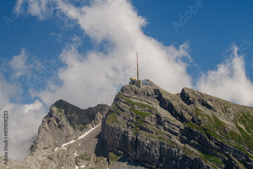View of a mountain peak  Säntis with a communication tower on top under a partly cloudy sky in the daytime