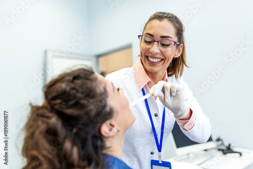 Fotografi Smiling female doctor performing throat examination on patient