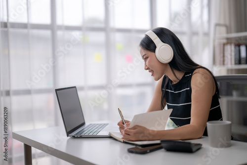Fotografia Young asian woman working from home attending online meeting taking notes