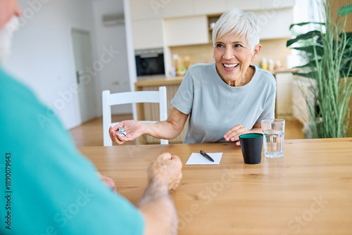 Portrait of a happy senior couple enjoying board game throwing dice at home