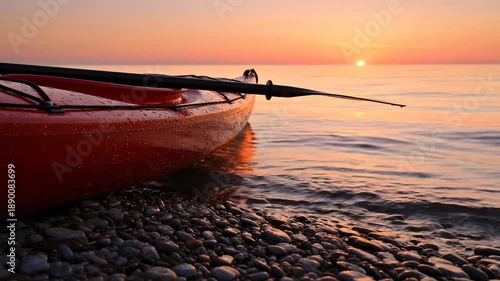 Orange kayak rests on a rocky beach at golden sunset, with calm waters gently lapping the shore. The serene scene evokes a profound sense of watersports tranquility and forthcoming adventure.