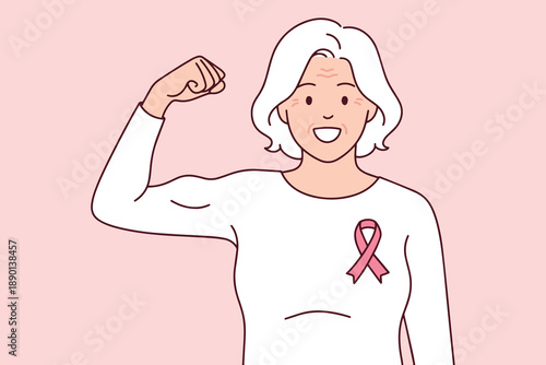 Courageous grandmother flexes her muscle while wearing a pink ribbon to symbolize strength over breast cancer. Inspiring portrait of age, resilience, and survival during awareness month.