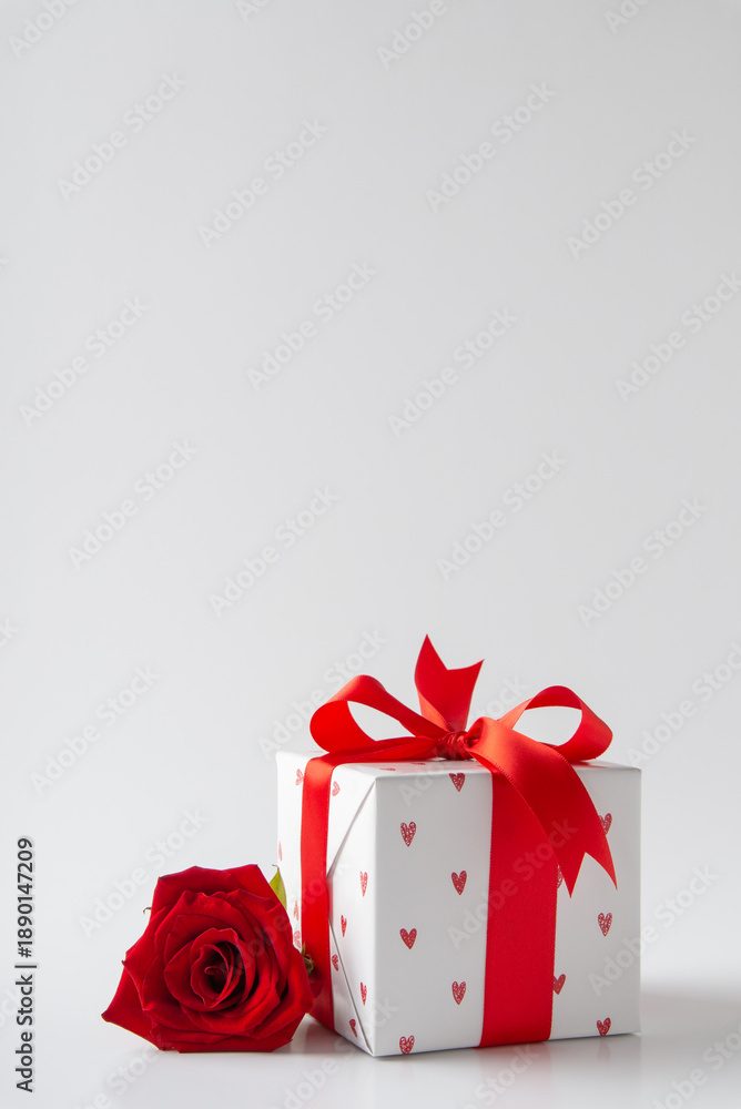 Obraz premium Gift, present box decorated with red ribbon bow and hearts, red rose flowers on white background. Valentine's day, February 14, birthday, 8 march women's day gift. Love and romance, valentines.