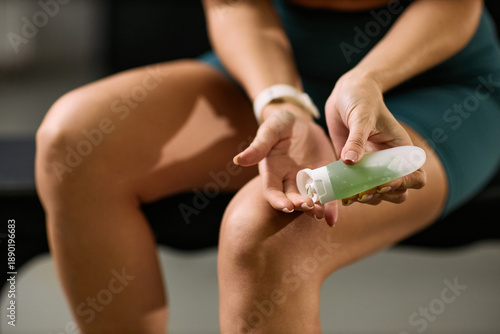 Bilde på lerret Young adult Caucasian woman applying topical gel to knee while sitting on bench,