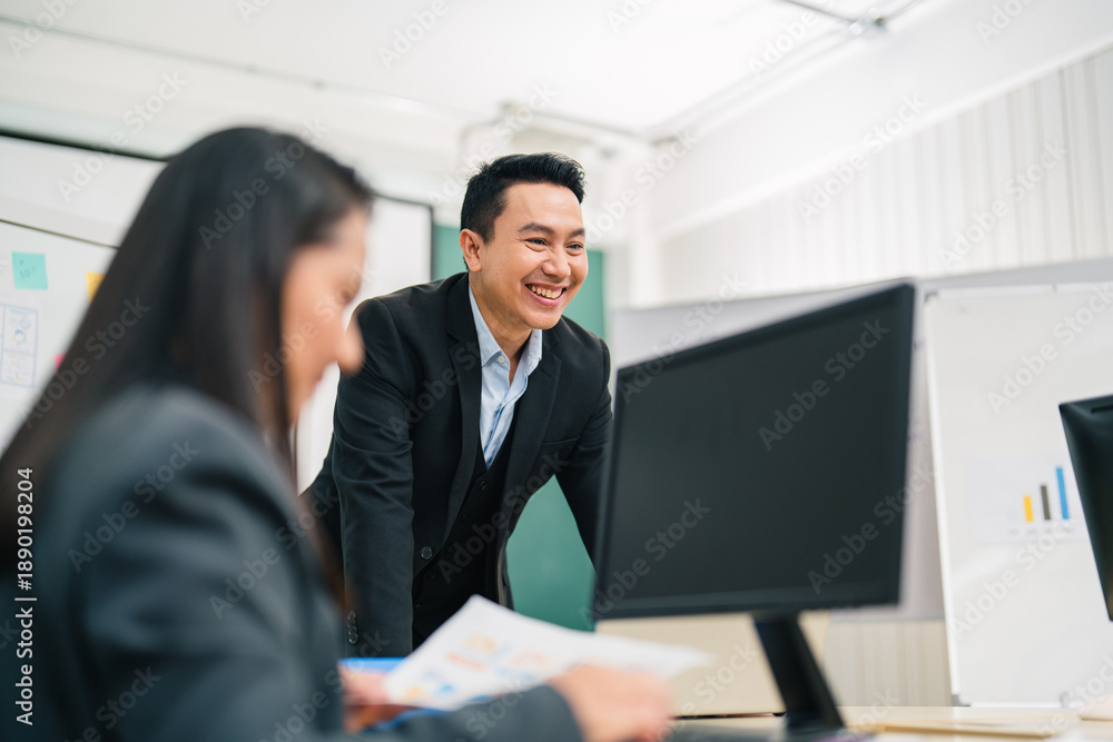 Naklejka premium Laughing Asian businessman leans over a boardroom table, leading a discussion and presentation with colleagues, communication, teamwork, leadership, and positive corporate culture