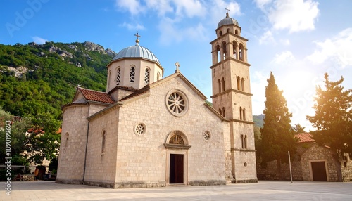 A stone church with a domed roof and bell tower, nestled against a mountain backdrop. Sunny with trees, sky