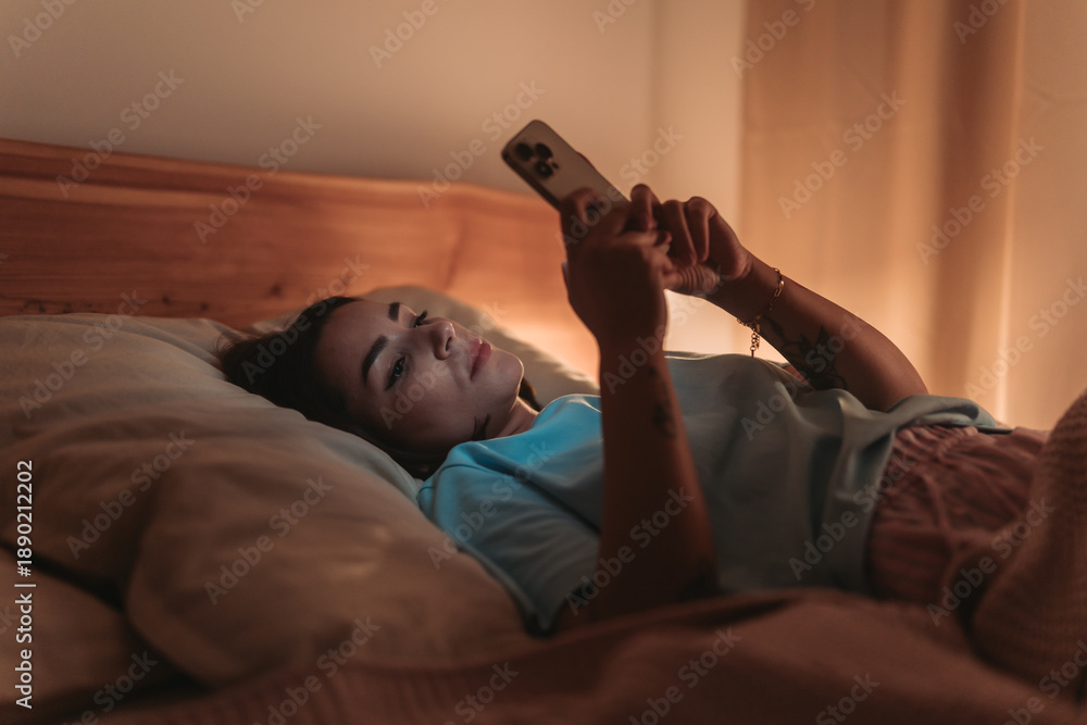 Fototapeta premium Woman Checks Email In Bed, Female Professional Works On Her Phone Amidst Restful Night Comfort