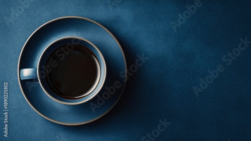 A refreshing cup of hot black coffee is presented in a deep blue ceramic cup with a matching saucer, all on a coordinating blue textured surface
