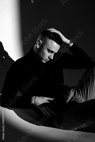 A portrait photo of a male model in a dark studio with window light. The handsome man wearing glasses looks into the camera. The businessman and his fashionable, elegant style