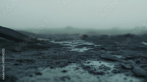 Wet dark muddy ground with small puddles under overcast gray sky, moody desolate landscape texture conveying foggy, dreary, gritty outdoor atmosphere and abandoned bleakness