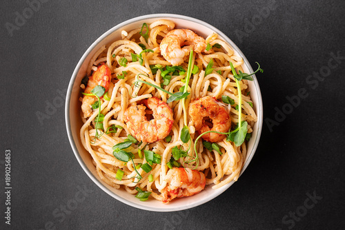 Spaghetti with cream sauce, parmesan, shrimps and onion, decorated with pea micro greens in white ceramic bowl on black stone background top view.