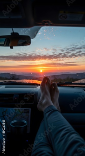 Serene sunset seen from inside car, legs relaxed on dashboard. The car's dashboard and the person's bare feet are visible, and the scenery depicts a scenic vista. 