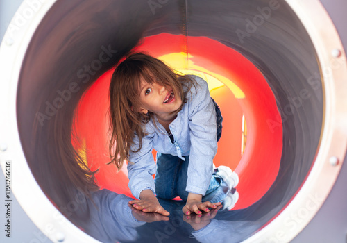 Adorable little girl crawling through playground tunnel slide, fun outdoor adventure, active child exploring colorful play equipment