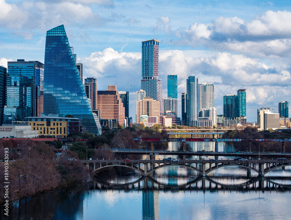 Fototapeta premium Clouds hover over the Austin skyline as buildings reflect on the calm waters of the Colorado river during late afternoon.