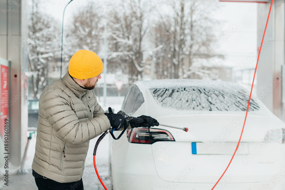 Fototapeta premium Man washing electric car at self-service car wash in winter