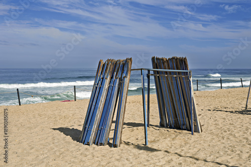 Beach scene in Furadouro featuring a circular structure made of upright wooden planks arranged like a shelter or windbreak.