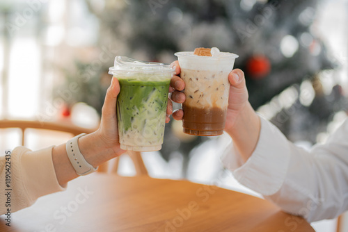 Hands of  female and male holding glass of ice coffee and ice matcha green tea together at cafe.