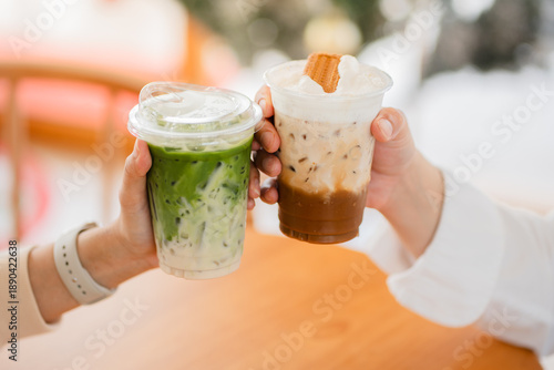 Foto Hands of  female and male holding glass of ice coffee and ice matcha green tea together at cafe