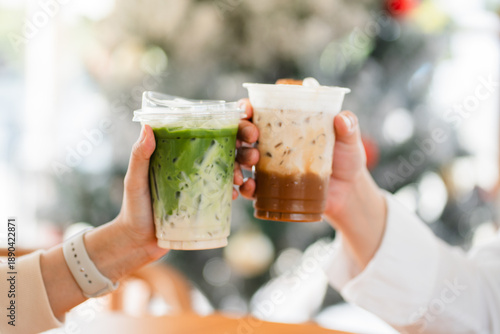 Hands of  female and male holding glass of ice coffee and ice matcha green tea together at cafe.