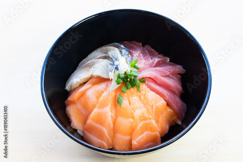 Mixed sashimi donburi rice bowl with fresh salmon, tuna, and mackerel slices topped with green onions. Traditional Japanese seafood meal, top view.