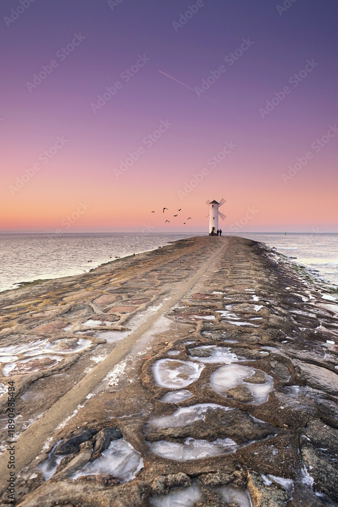 Fototapeta premium lighthouse on a stone pier in sunset light in winter season