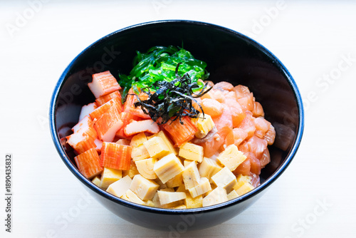 Donburi rice bowl topped with savory sauce, shredded nori, sesame seeds, and green onions. Hearty Japanese meat meal, top view.