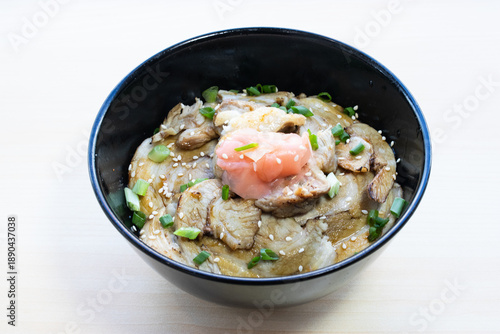 Japanese Butadon rice bowl topped with grilled pork slices, savory soy glaze, pickled ginger, and green onions. Hearty meat meal, top view close-up.
