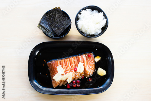 Korean-style pickled salmon in soy sauce with garlic and chili, served with steamed rice and dried seaweed nori. Asian seafood set meal, top view.