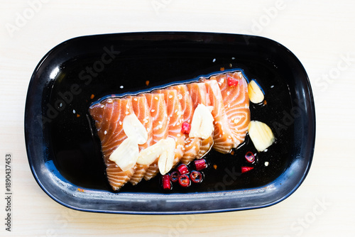 Korean-style pickled salmon slices in savory soy sauce topped with fresh garlic, chili, and sesame seeds. Traditional Asian seafood dish, top view.