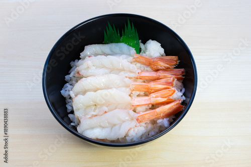 Japanese Ama Ebi Donburi featuring fresh raw sweet shrimp on rice, garnished with green plastic leaf. Traditional seafood sushi bowl, top view.