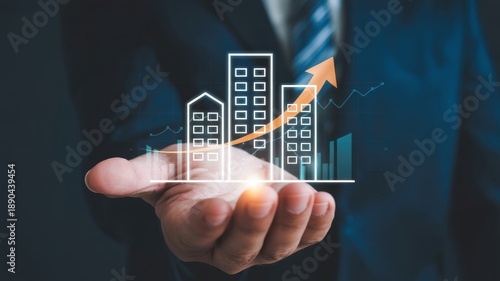 A businessman's hand cradles a glowing projection of modern buildings with an upward arrow, symbolizing successful real estate market growth, increasing property value, and strategic investment.