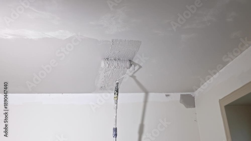Close up view of paint roller applying fresh gray primer on ceiling corner after sanding and plaster preparation during interior renovation. Sweden.