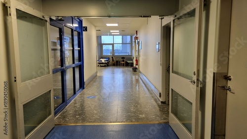 Fotografía Hospital corridor features open double doors leading to a hallway with white walls and a blue linoleum floor